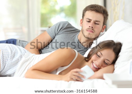 Jealous gossip husband watching his wife mobile phone on the bed at home Royalty-Free Stock Photo #316154588