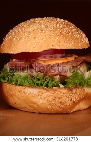 One appetizing big delicious fresh burger with green lettuce red tomato cheese cabbage bacon slice meat cutlet and white bread bun with sesame seeds on black background closeup, vertical picture