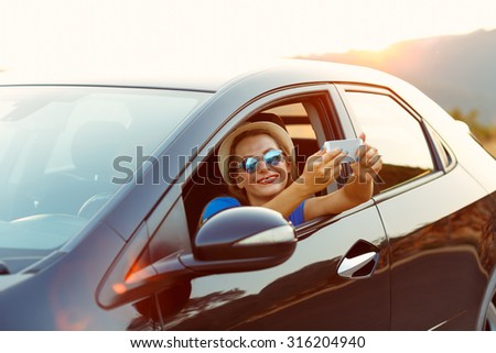 Young smiling woman in hat and sunglasses making self portrait sitting in the car