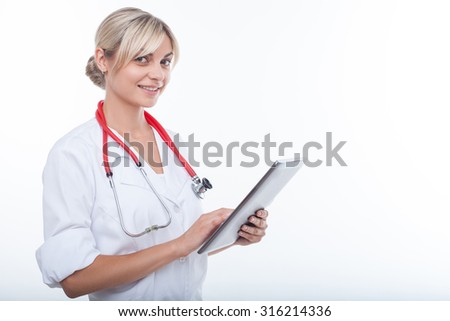 Beautiful doctor is using a tablet for her work. The woman is looking at the camera with joy. She is standing and smiling. Isolated and copy space in right side
