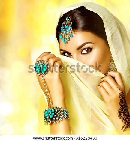 Arabian woman portrait. Arab girl with oriental jewellery and make-up hiding her face behind a veil and smiling. Brunette Hindu model girl with Indian jewels. Traditions