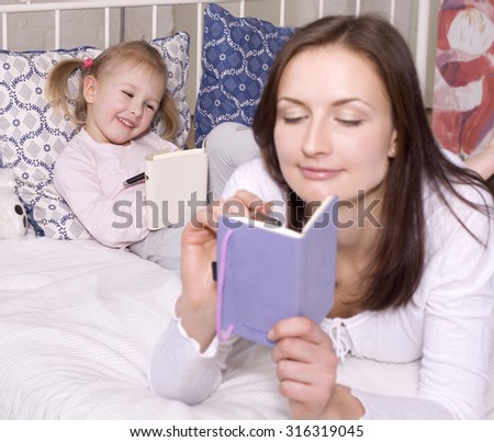portrait of mother and daughter laying in bed reading book smiling