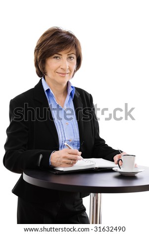 Senior businesswoman standing at coffee table, writing notes, smiling and looking at camera. Isolated on white background.