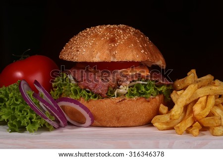 One big tasty appetizing fresh burger of green lettuce red tomato cheese bacon slice meat cutlet violet onion and white bread bun with sesame seeds on black backgeound closeup, horizontal picture