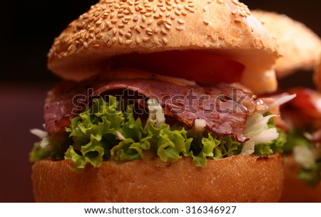 One big tasty appetizing fresh burger of green lettuce red tomato cheese and bacon slice and white bread bun with sesame seeds closeup, horizontal picture