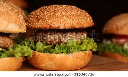 Few big delicious appetizing fresh burgers of green lettuce leaf cheese meat cutlet and white bread bun with sesame seeds on black background closeup, horizontal picture
