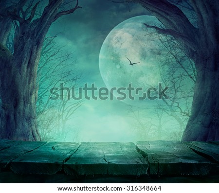 Halloween background. Spooky forest with full moon and wooden table
