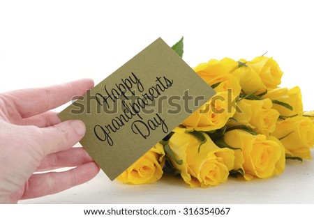Yellow roses gift for Grandparents Day with older womans hand holding greeting card, on white vintage wood table. 