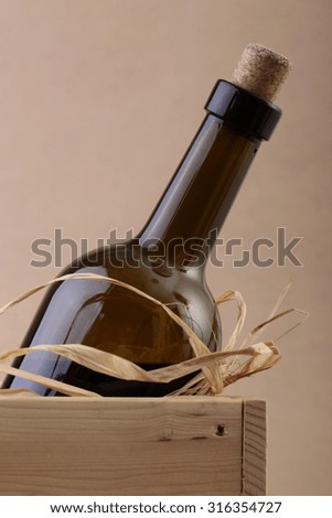 Closeup photo of uncorked not full dark glass bottle of vintage red wine in wooden box with straw, vertical picture