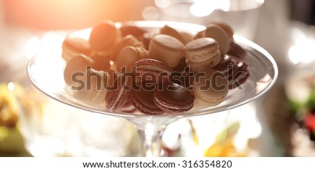 Many small round traditional french sweet cookies of macaron white and brown colors vanilla and chocolate lying in glass plate sunny day, horizontal picture