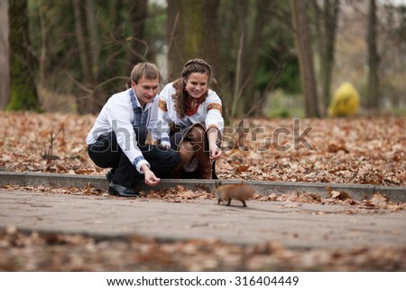 beautiful ukrainian bride and groom in native embroidery suits feeding cute squirrel  on the background of trees in a park, traditional wedding ceremony