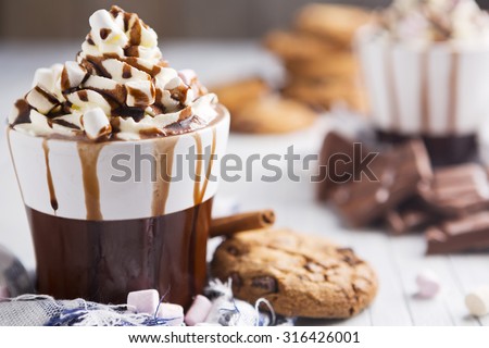 A messy cup with hot chocolate, whipped cream, marshmallows and chocolate chip cookies.