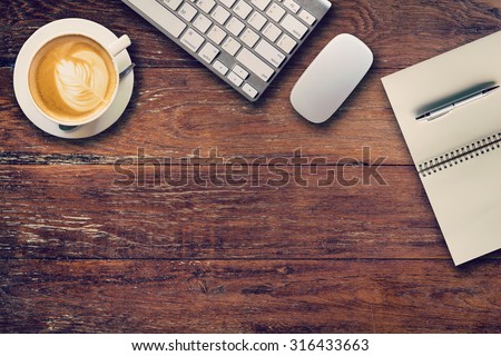 Office table with computer, notebook and coffee cup. View from above for vintage tone.