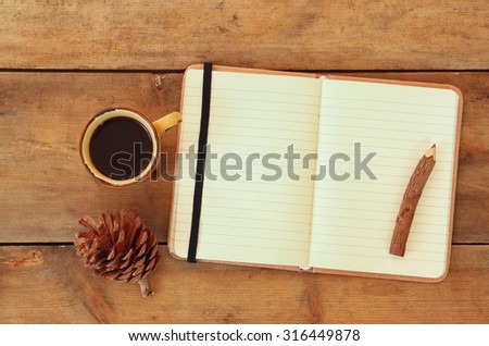top image of open notebook with blank pages, next to pine cones and cup of coffee over wooden table. 