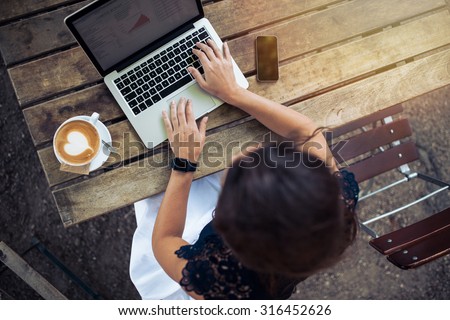Top view of female using her laptop at a cafe. Overhead shot of young woman sitting at a table with a cup of coffee and mobile phone surfing the net on her laptop computer. Royalty-Free Stock Photo #316452626