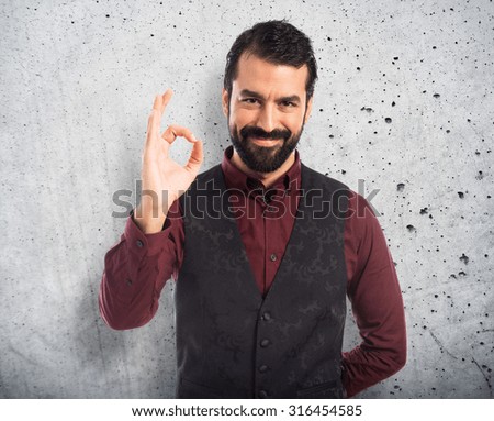 Man wearing waistcoat making Ok sign over textured background