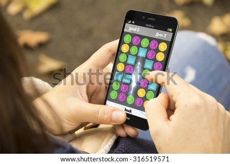 idle and gaming concept: girl playing a jigsaw game on a digital generated smartphone. All screen graphics are made up. Royalty-Free Stock Photo #316519571