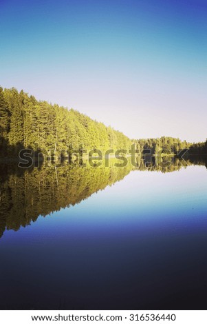 Beautiful and peaceful evening by the lake. The colorful forest makes a nice reflection on a still water. Image has a vintage effect applied.