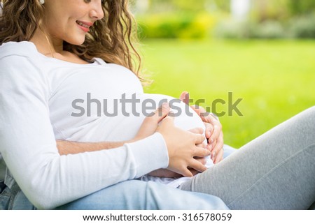 Happy and young pregnant couple in park in summer