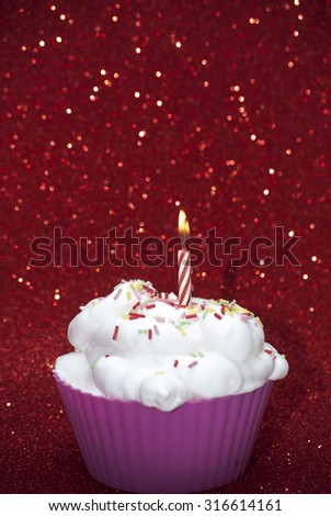 Cupcake with a lit candle over bright red background