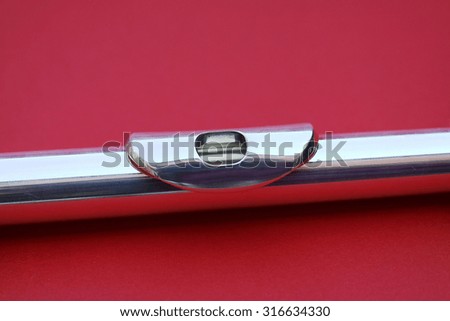 Silver flute mouthpiece in front of a red background