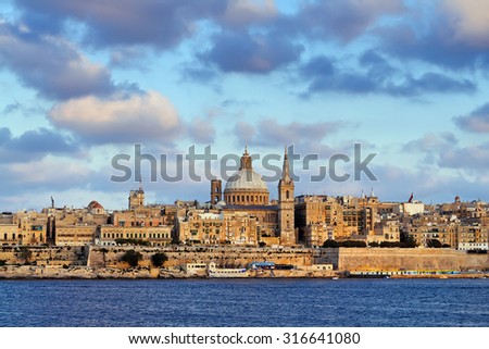 View from Sliema over Marsamxett Harbour to La Valletta, the capital city of Malta, under cloudy sky in warm evening light.