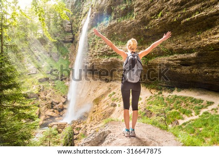 Female hiker raising arms inhaling fresh air, feeling relaxed and free in beautiful natural environment under Pericnik waterfall in Vrata Valley in Triglav National Park in Julian Alps, Slovenia. Royalty-Free Stock Photo #316647875