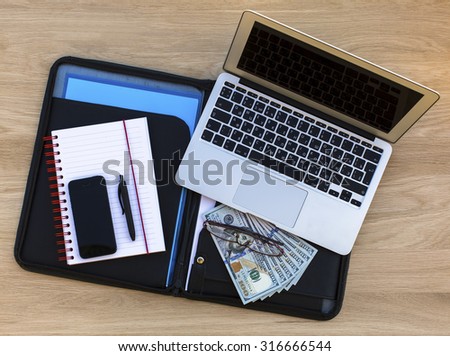 Business concept - folder for documents, laptop, glasses, Notepad with pen and hundred-dollar bills - a top view on the table of expensive wood.