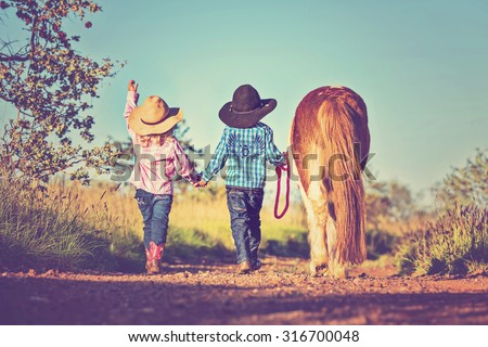 Little cowboy and cowgirl walking pony