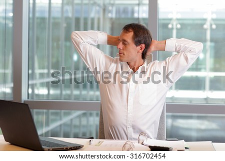 white collar worker male stretching arms, relaxing neck - short break for exercise on chair in office Royalty-Free Stock Photo #316702454