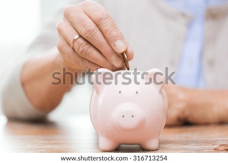 savings, money, annuity insurance, retirement and people concept - close up of senior woman hand putting coin into piggy bank Royalty-Free Stock Photo #316713254