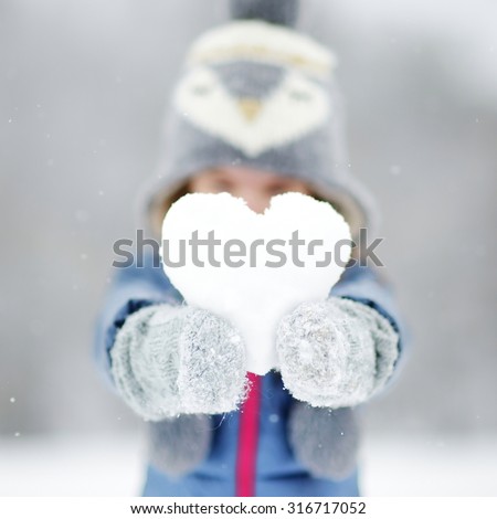 Funny little girl holding snow heart in beautiful winter park during snowfall