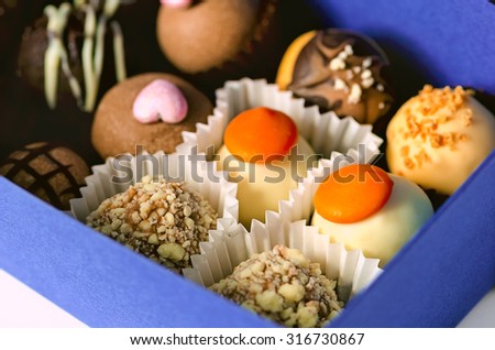 Handmade chocolate candies into the blue gift box on the white background, toned