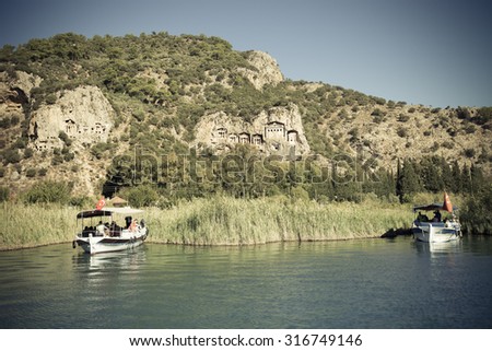 Two touristic boats on the background of Lycian Tombs of ancient Caunos city, Dalyan, Turkey. Toned.