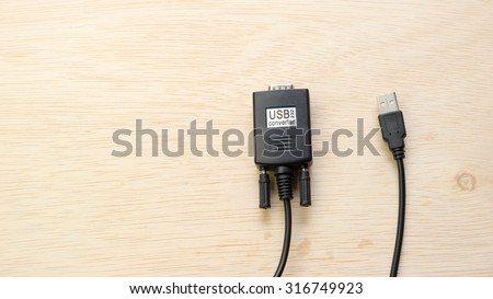 Black color usb to 9 pin RS-232 serial port cable converter adapter on wooden surface. Slightly de-focused and close-up shot. Copy space.