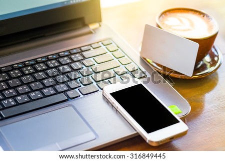 empty smart phone and empty business card in coffee shop cafe on wooden desk for online shopping.selective focus .vintage tone Retro filter effect,soft focus,low light.