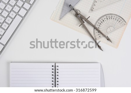 Top view mock up of a white drafting table with computer keyboard, compass, protractor and angle open notebook and graph paper. Horizontal format with copy space.