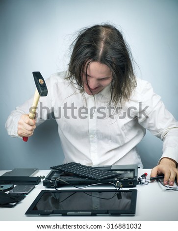 Crazy psycho shaggy man in white shirt thinking to keep his head in the disassembled parts broken laptop lying on a white table