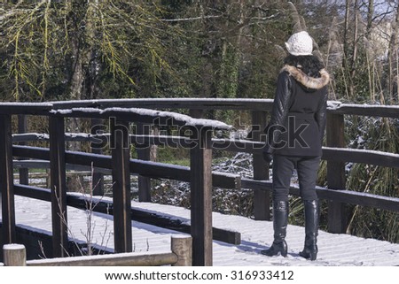 Woman crossing a bridge snowed in the cold day of winter. Stock photography.