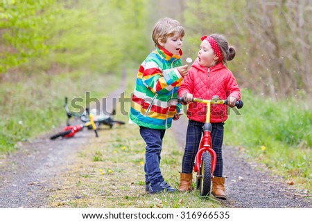 Little girl and boy playing together in forest in bright jackets on a rainy day with bikes. Friendship between siblings. Happy family concept 