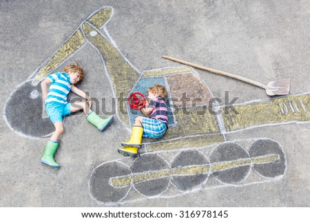 Two little happy kid boys having fun with excavator picture drawing with colorful chalk. Creative leisure for children outdoors in summer.