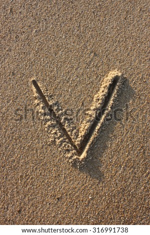 Alphabet's letter V handwritten in sand on the beach, at sunrise.