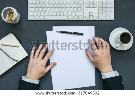 Businessman writing a letter at office working table with notepad, computer and cup of coffee. Top view.
