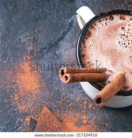 Vintage mug of hot chocolate with cinnamon sticks over dark background. Top view. Square image with selective focus.