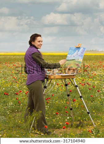 woman artist paints picture with brush  on the poppy field