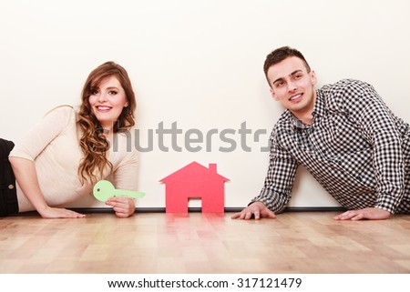 Smiling young couple laying on floor holding paper house and key. Husband and wife dreaming about new home. Housing and real estate concept.