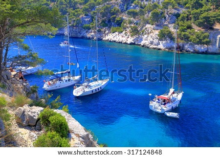 Sail boats surrounded by tall cliffs inside one of the calanques near Cassis, France Royalty-Free Stock Photo #317124848