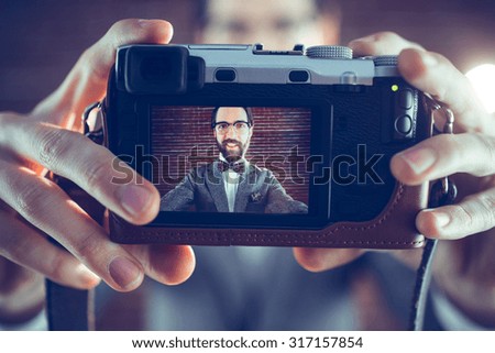 Smiling hipster taking self portrait through camera against brick wall