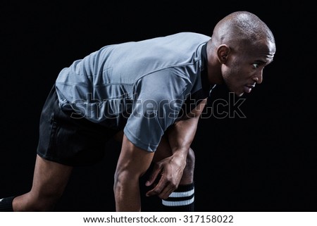 Determined sportsman bending while playing rugby against black background