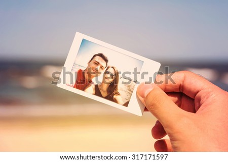 Retro Photo Of Man Hand Holding Instant Photo Of Happy Couple On Beach